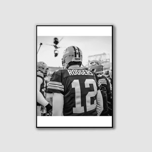 May include: Black and white photograph of a football player wearing a green and white jersey with the number 12 and the name "RODGERS" on the back. The player is standing with other players in the background.