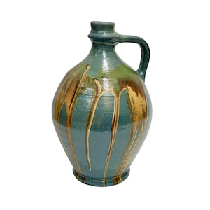 May include: A teal-colored ceramic jug with a handle. The jug has a rounded body and a narrow neck. Brown and gold glaze drips down the sides, creating a unique, textured appearance. The jug is likely handmade and suitable for decorative use.