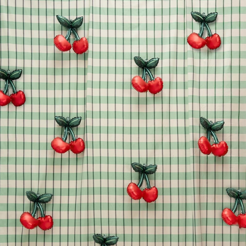K&ouml;nnte beinhalten: Ein sich wiederholendes Muster aus roten kirschf&ouml;rmigen Luftballons mit gr&uuml;nen Stielen und Bl&auml;ttern auf einem hellgr&uuml;nen und wei&szlig;en karierten Hintergrund. Die Ballons sind &uuml;ber den Stoff verteilt und erzeugen ein fr&ouml;hliches Design.