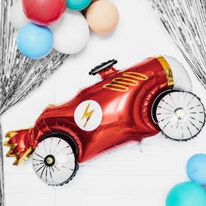 May include: A red and gold foil balloon shaped like a race car with a white lightning bolt on the side. The balloon has white wheels with black spokes.