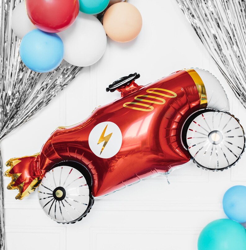 May include: A red and gold foil balloon shaped like a race car with a white lightning bolt on the side. The balloon has white wheels with black spokes.