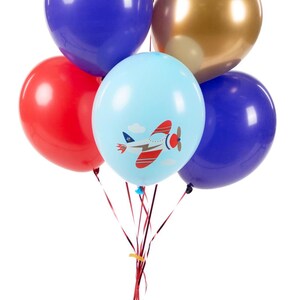 K&ouml;nnte beinhalten: Ein B&uuml;ndel Ballons, die mit rotem Lockenband zusammengebunden sind. Die Ballons sind blau, rot, gold und hellblau mit einem roten Flugzeugdesign.
