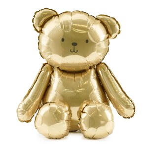 May include: A large, gold-colored teddy bear balloon. The balloon has a classic teddy bear shape with a small face and limbs. The balloon is inflated and ready for a party or celebration.