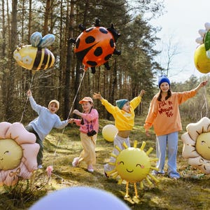 Puede incluir: Cuatro ni&ntilde;os en un entorno de bosque sosteniendo decoraciones de globos coloridos. Los globos tienen forma de mariquita, abeja, sol y dos flores. Los ni&ntilde;os visten ropa informal y sonr&iacute;en. Un ni&ntilde;o sostiene un globo que dice "I'll be Wonder Full".