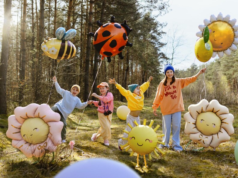 Puede incluir: Cuatro ni&ntilde;os en un entorno de bosque sosteniendo decoraciones de globos coloridos. Los globos tienen forma de mariquita, abeja, sol y dos flores. Los ni&ntilde;os visten ropa informal y sonr&iacute;en. Un ni&ntilde;o sostiene un globo que dice "I'll be Wonder Full".
