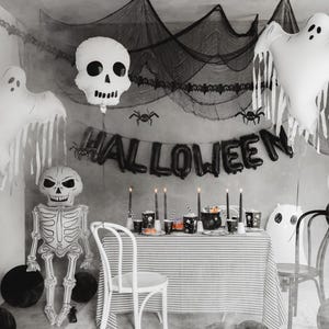 Black and white Halloween party setup with large ghost balloon, skeleton decor and spooky backdrop