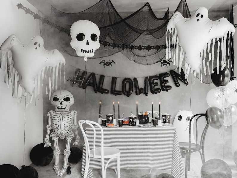 Black and white Halloween party setup with large ghost balloon, skeleton decor and spooky backdrop