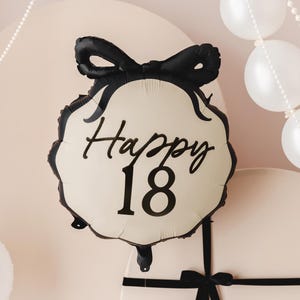 May include: A white and black balloon with a black bow and the text "Happy 18" printed on it.