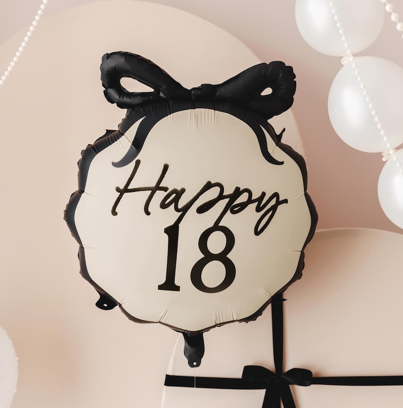 May include: A white and black balloon with a black bow and the text "Happy 18" printed on it.