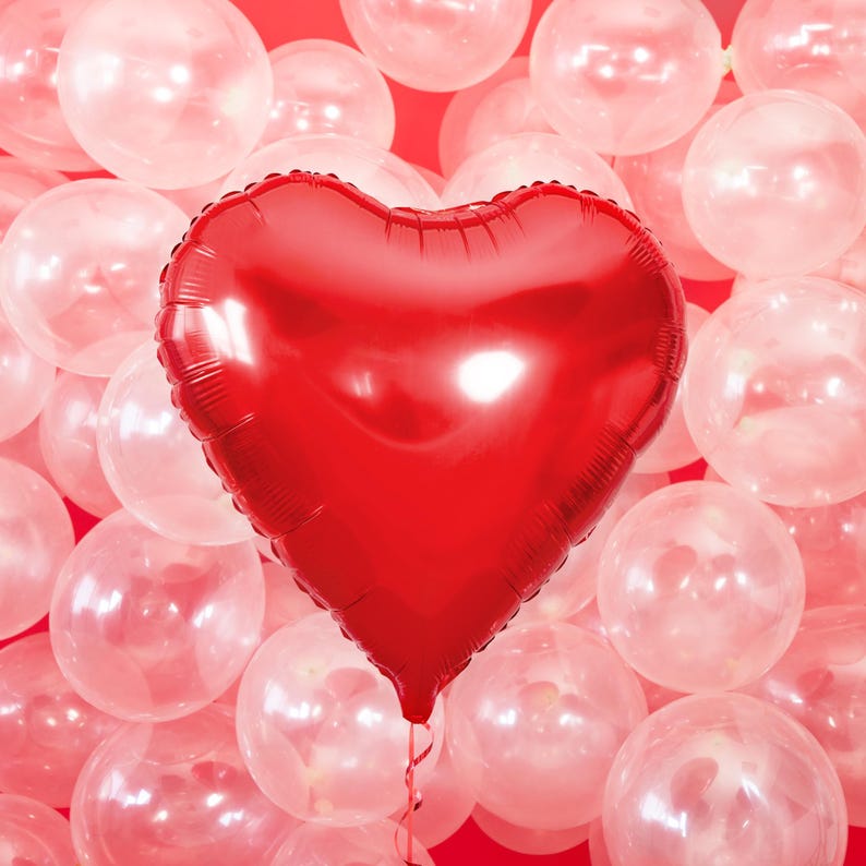 Red heart foil balloon with pink clear balloons background – romantic Valentine’s Day party decor or wedding photo backdrop