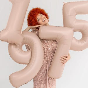 Beige number balloons held as a birthday photo prop, large neutral number decoration for milestone celebrations