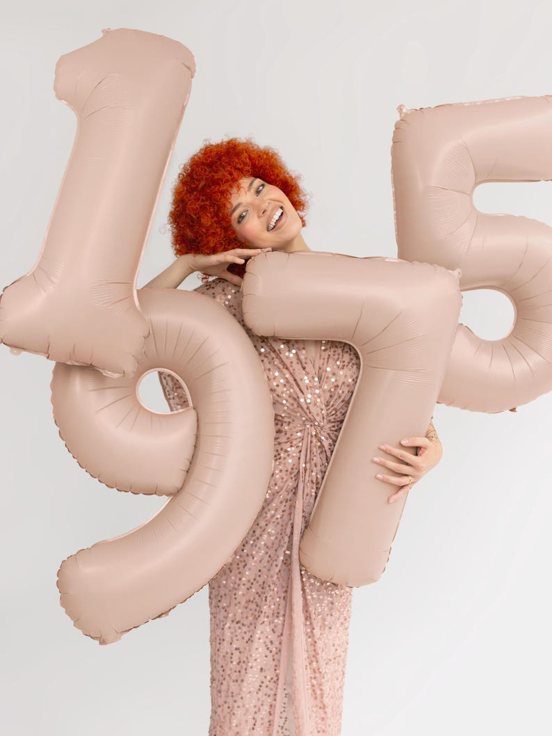 Beige number balloons held as a birthday photo prop, large neutral number decoration for milestone celebrations
