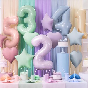 May include: Pastel colored foil balloons in the shape of stars and numbers 2, 3, 4, and 5. The balloons are decorated for a birthday party with two cakes and other decorations.