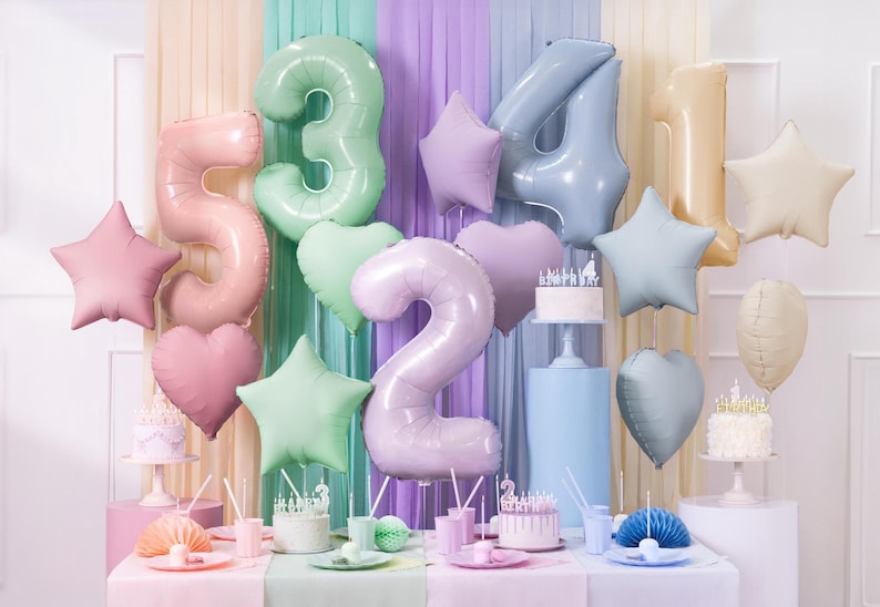 May include: Pastel colored foil balloons in the shape of stars and numbers 2, 3, 4, and 5. The balloons are decorated for a birthday party with two cakes and other decorations.