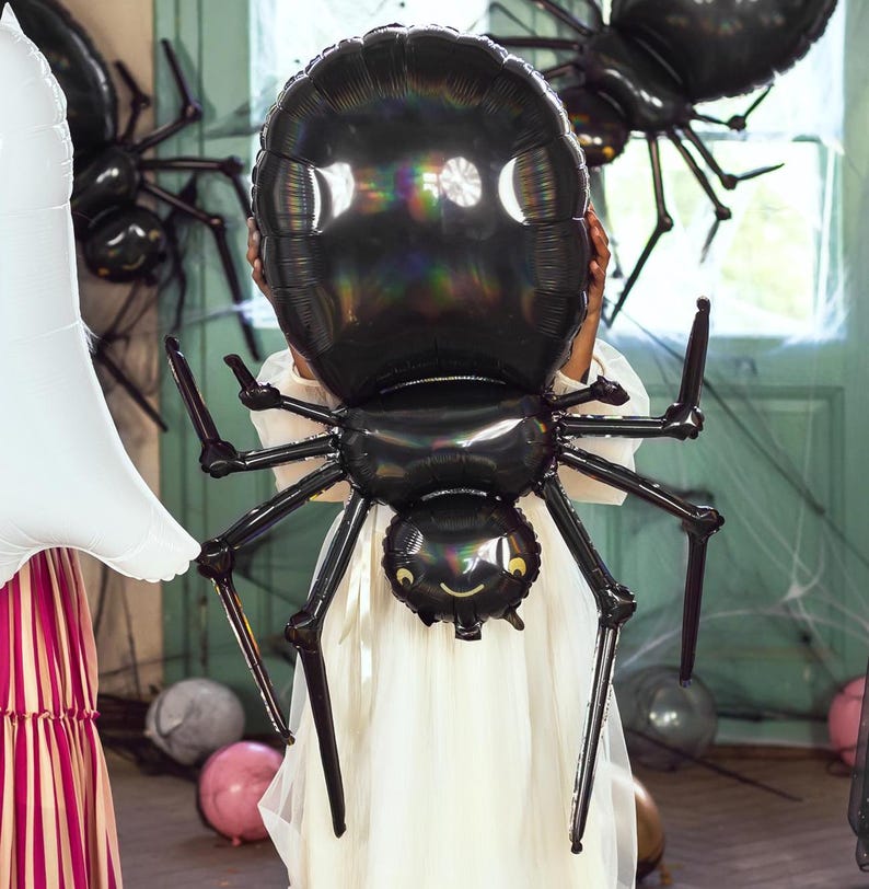Op de afbeelding: Een grote zwarte iriserende spinballon met een glimlachend gezicht. De ballon wordt vastgehouden door een persoon die een witte jurk draagt.