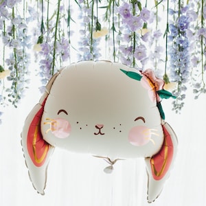 May include: A white balloon shaped like a bunny with red and gold ears. The balloon has a cute face with pink cheeks and a small black nose. The balloon is decorated with a green leaf and a pink flower.