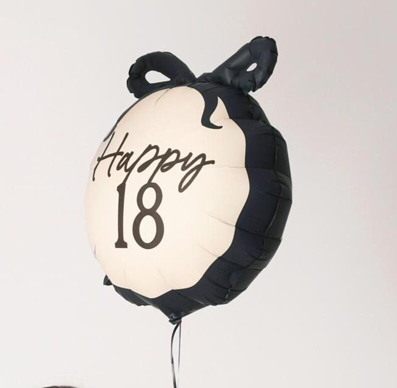 May include: Black and white balloon with a bow on top. The balloon has the text "Happy 18" printed on it.