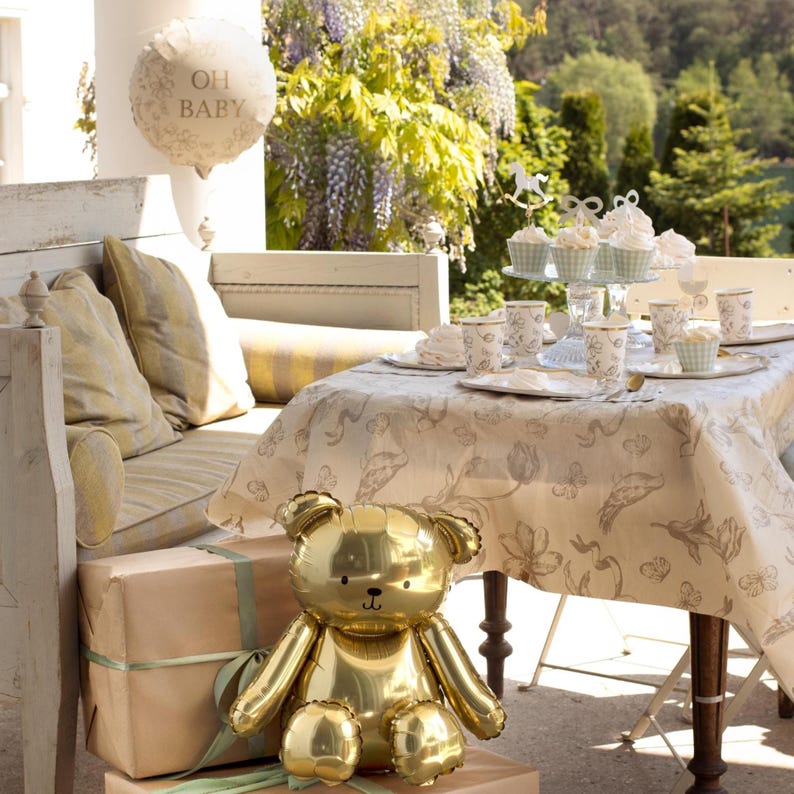 Puede incluir: Un globo dorado con forma de oso de peluche est&aacute; sobre regalos envueltos con cinta verde. Una mesa est&aacute; puesta con cupcakes, tazas y platos. Un globo con el texto "OH BABY" flota encima, sugiriendo un baby shower.