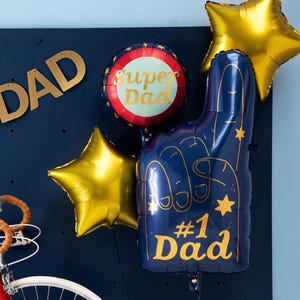 May include: A collection of festive balloons in gold, blue, and red, perfect for a Father's Day celebration. The arrangement includes star-shaped balloons, a foam finger balloon with "#1 Dad" text, and a round balloon with "Super Dad" text.