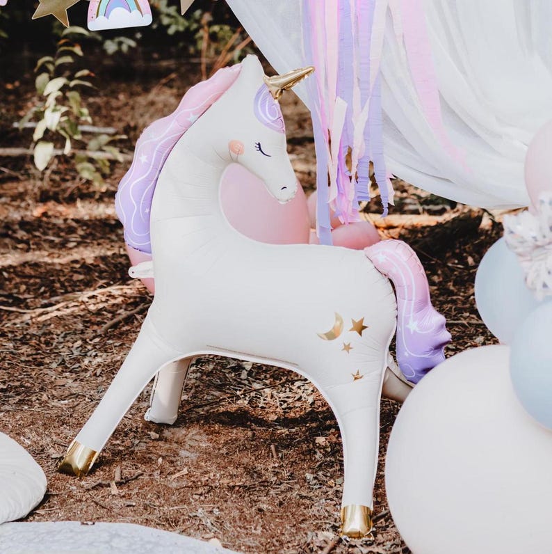 K&ouml;nnte beinhalten: Ein wei&szlig;es aufblasbares Einhorn mit goldenem Horn und Hufen. Das Einhorn hat eine rosa und lila M&auml;hne und einen Schweif sowie goldene Mond- und Sternakzente. Das Einhorn ist Teil eines Party-Dekorationssets.