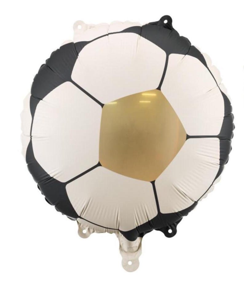 May include: A soccer ball-shaped foil balloon. The balloon features a classic soccer ball design with white pentagons, black hexagons, and a gold-colored pentagon in the center. It has a shiny, metallic finish and is designed for party decorations.