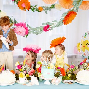 Op de afbeelding: Een feestelijke Paassc&egrave;ne met kinderen en decoraties. Een jongen in een bruine trui en kinderen met bloemenhoeden verzamelen zich rond een tafel met een taart, bloemen en een kuikenvormige ballon. De tafel is versierd met wortels en papieren decoraties.
