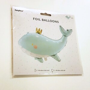 Może przedstawiać: Jasnoniebieski balon foliowy w kształcie wieloryba z złotą koroną na głowie. Balon ma białe kropki i r&oacute;żowy rumieniec na policzku. Opakowanie zawiera napis "FOIL BALLOONS" i podaje wymiary balonu w calach i centymetrach.