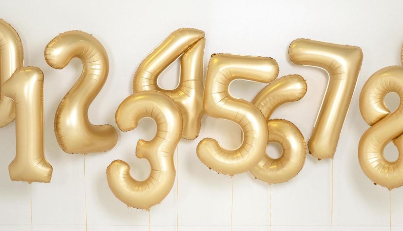 May include: Gold foil number balloons, including the numbers 1, 2, 3, 4, 5, 6, 7, and 8. The balloons are inflated and tied together.