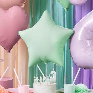 May include: A green star-shaped foil balloon with a white cake decorated with candles that spell out "Happy Birthday" and a number three candle.