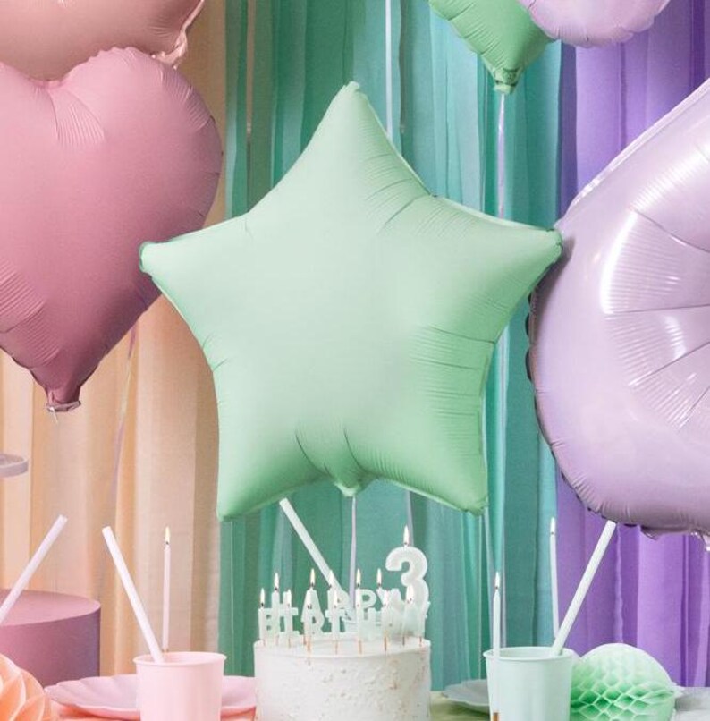 May include: A green star-shaped foil balloon with a white cake decorated with candles that spell out "Happy Birthday" and a number three candle.