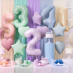 May include: A pastel-colored birthday party decoration set with foil balloons in the shape of numbers, stars, and hearts. The balloons are in shades of pink, blue, green, and gold.