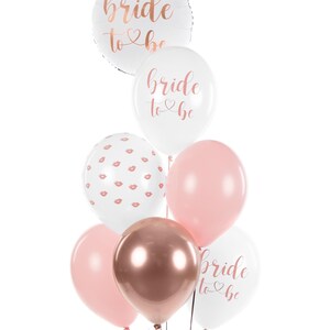 May include: A bouquet of balloons for a bridal shower or bachelorette party. The balloons are white, pink, and rose gold. Some of the balloons have the text "bride to be" printed on them in rose gold lettering. One balloon has a pattern of pink lips on a white background.
