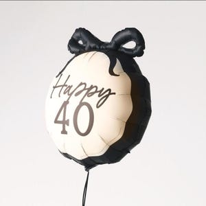 May include: A round, black and cream-colored balloon with the words "Happy 40" printed on it. The balloon has a black bow at the top and a black string at the bottom. This festive balloon is perfect for a 40th birthday celebration.