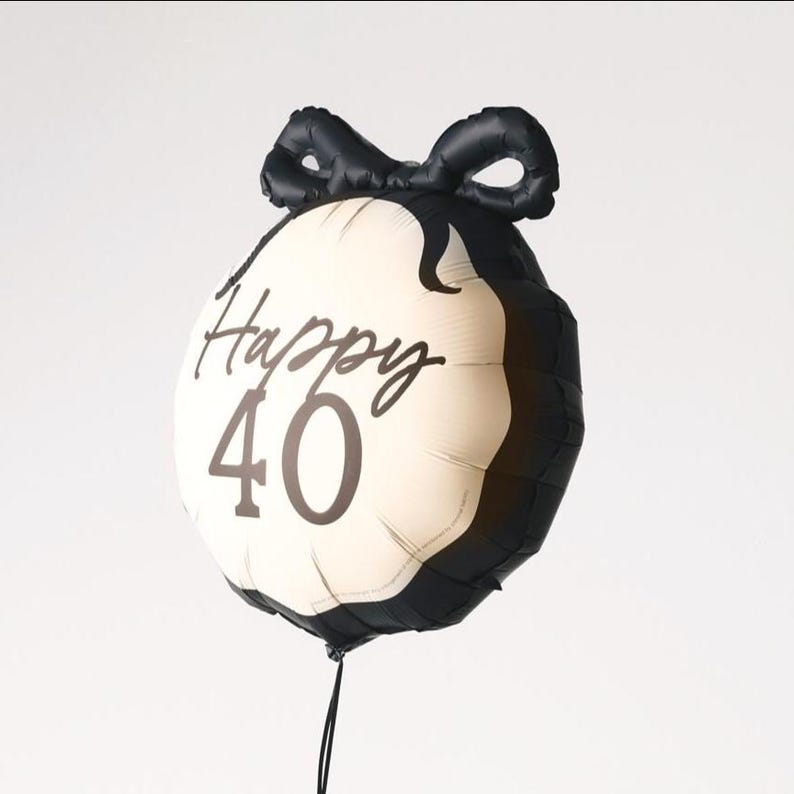 May include: A round, black and cream-colored balloon with the words "Happy 40" printed on it. The balloon has a black bow at the top and a black string at the bottom. This festive balloon is perfect for a 40th birthday celebration.