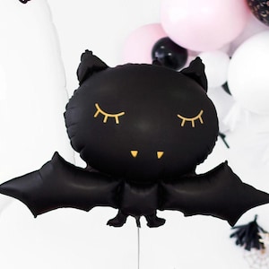 以下が含まれることがあります： 金色のまつげと小さな笑顔をした黒いコウモリの風船。風船は膨らませてあり、ハロウィーンパーティーや飾り付けに使うことができます。