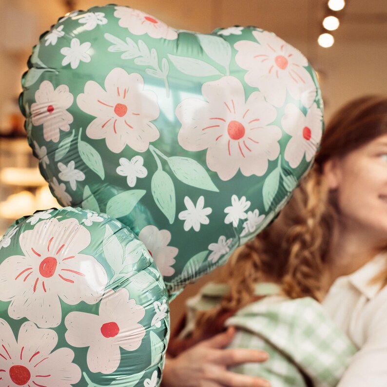 May include: Two heart-shaped balloons with a floral pattern in shades of green and white. The balloons are partially overlapping.