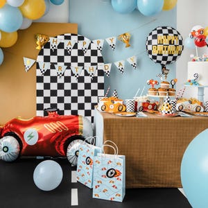 May include: A birthday party table setting with a checkered black and white backdrop. The table is decorated with a checkered tablecloth, red and white checkered paper plates, and red and white checkered cups. There are also red and white checkered party hats, a red and white checkered balloon, and a red and white checkered cake. The table is set for a birthday party with a racing car theme.