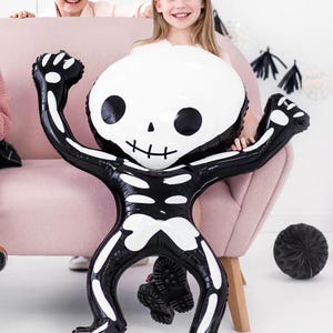 Puede incluir: Un gran globo de esqueleto negro y blanco con una cara amigable. El globo est&aacute; sentado en un sof&aacute; rosa con dos ni&ntilde;os detr&aacute;s.