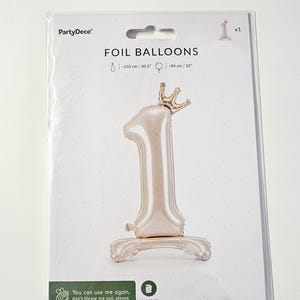 K&ouml;nnte beinhalten: Ein goldener Folienballon in Form der Zahl eins mit einer goldenen Krone oben drauf. Der Ballon ist 103 cm hoch und 84 cm breit. Die Verpackung tr&auml;gt die Aufschrift "FOIL BALLOONS" und "PartyDeco".