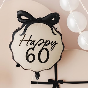 May include: A cream-coloured balloon with a black bow and the text "Happy 60" in black script.
