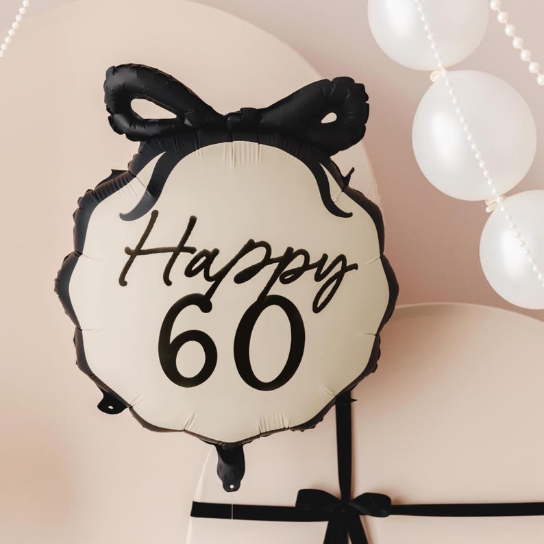 May include: A cream-coloured balloon with a black bow and the text "Happy 60" in black script.