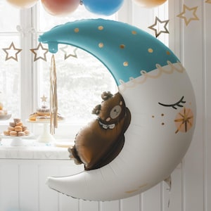 May include: A large blue and white crescent moon balloon with gold stars and dots. A brown bear balloon is nestled inside the moon balloon.