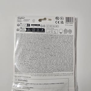 May include: A warning label for a package of balloons. The label is printed in multiple languages and includes safety information about choking hazards, suffocation, and electric power lines. The label also states that colors may stain or bleed when wet.