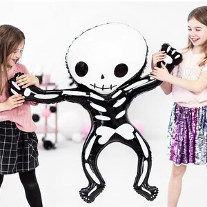 Puede incluir: Dos ni&ntilde;os juegan con un gran globo de esqueleto negro y blanco. El globo tiene forma de persona y tiene una cara de calavera. Los ni&ntilde;os sonr&iacute;en y se divierten.