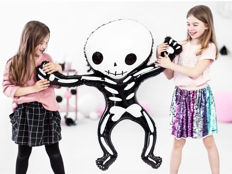 Puede incluir: Dos ni&ntilde;os juegan con un gran globo de esqueleto negro y blanco. El globo tiene forma de persona y tiene una cara de calavera. Los ni&ntilde;os sonr&iacute;en y se divierten.