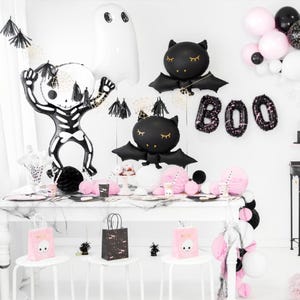 Puede incluir: Decoraciones de fiesta de Halloween en blanco y negro con un esqueleto, murci&eacute;lagos y fantasmas. Las decoraciones est&aacute;n sobre una mesa blanca con manteles blancos y negros. La mesa est&aacute; puesta con platos, vasos y servilletas blancos y negros. Tambi&eacute;n hay globos y serpentinas blancos y negros. La palabra "BOO" est&aacute; escrita en globos negros.