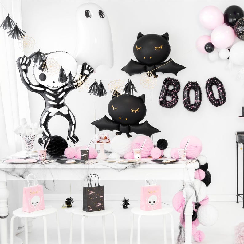 Puede incluir: Decoraciones de fiesta de Halloween en blanco y negro con un esqueleto, murci&eacute;lagos y fantasmas. Las decoraciones est&aacute;n sobre una mesa blanca con manteles blancos y negros. La mesa est&aacute; puesta con platos, vasos y servilletas blancos y negros. Tambi&eacute;n hay globos y serpentinas blancos y negros. La palabra "BOO" est&aacute; escrita en globos negros.