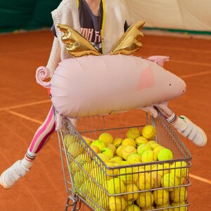 Flying pig balloon with gold wings displayed above a shopping cart, playful pink party decoration for birthdays