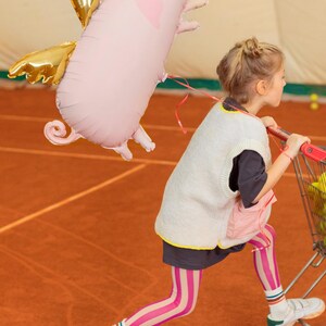 Large pink flying pig balloon with gold wings shown with a child, whimsical birthday and kids party decoration
