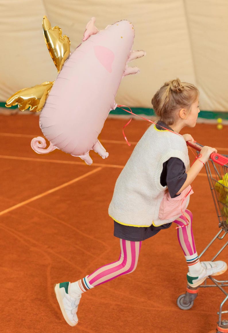 Large pink flying pig balloon with gold wings shown with a child, whimsical birthday and kids party decoration